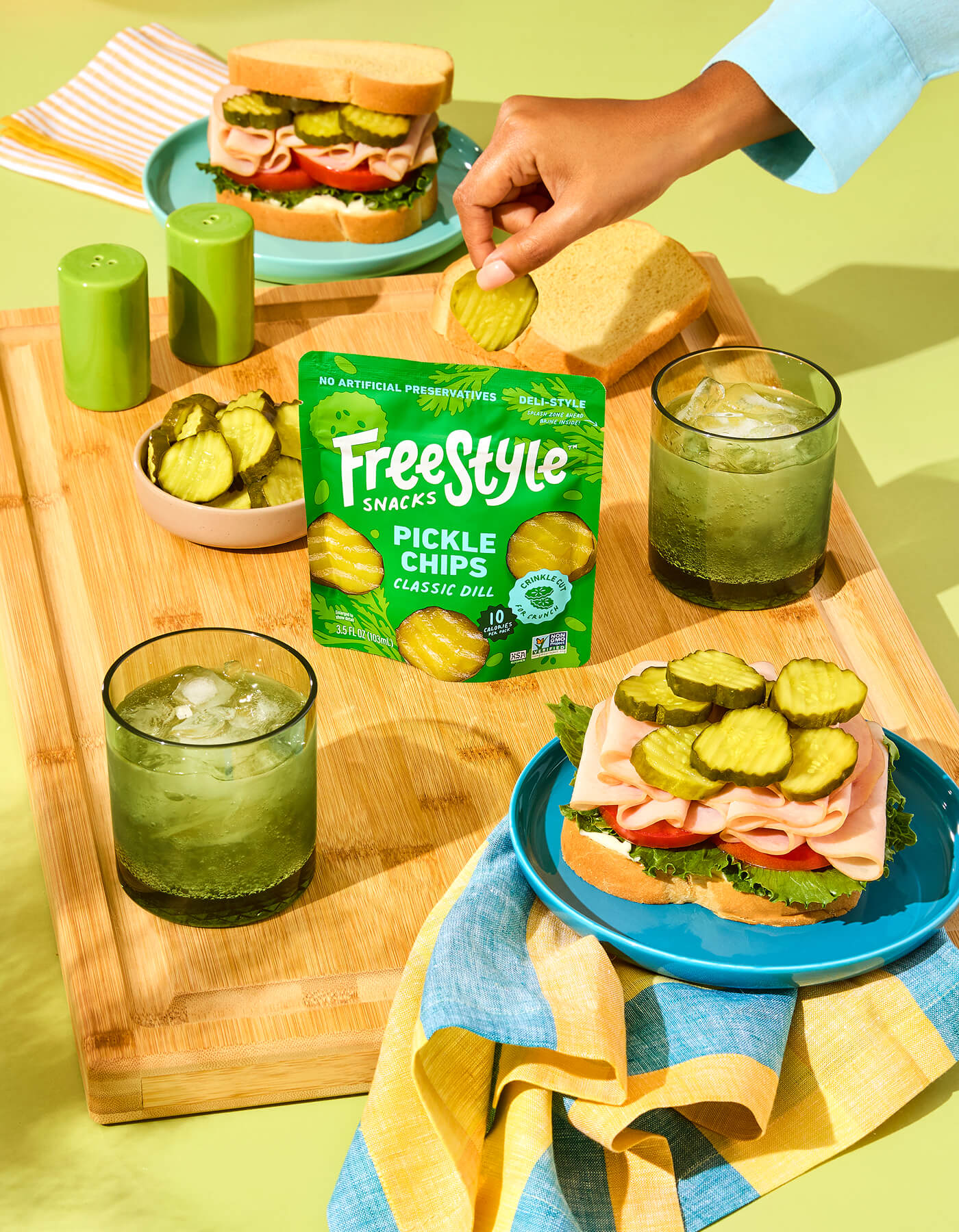 Freestyle Snacks Pickle Chips Classic Dill packaging with sandwiches and drinks on a wooden board.