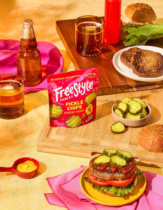 Freestyle Snacks Pickle Chips Kickin' Picks package on a table with burgers and drinks