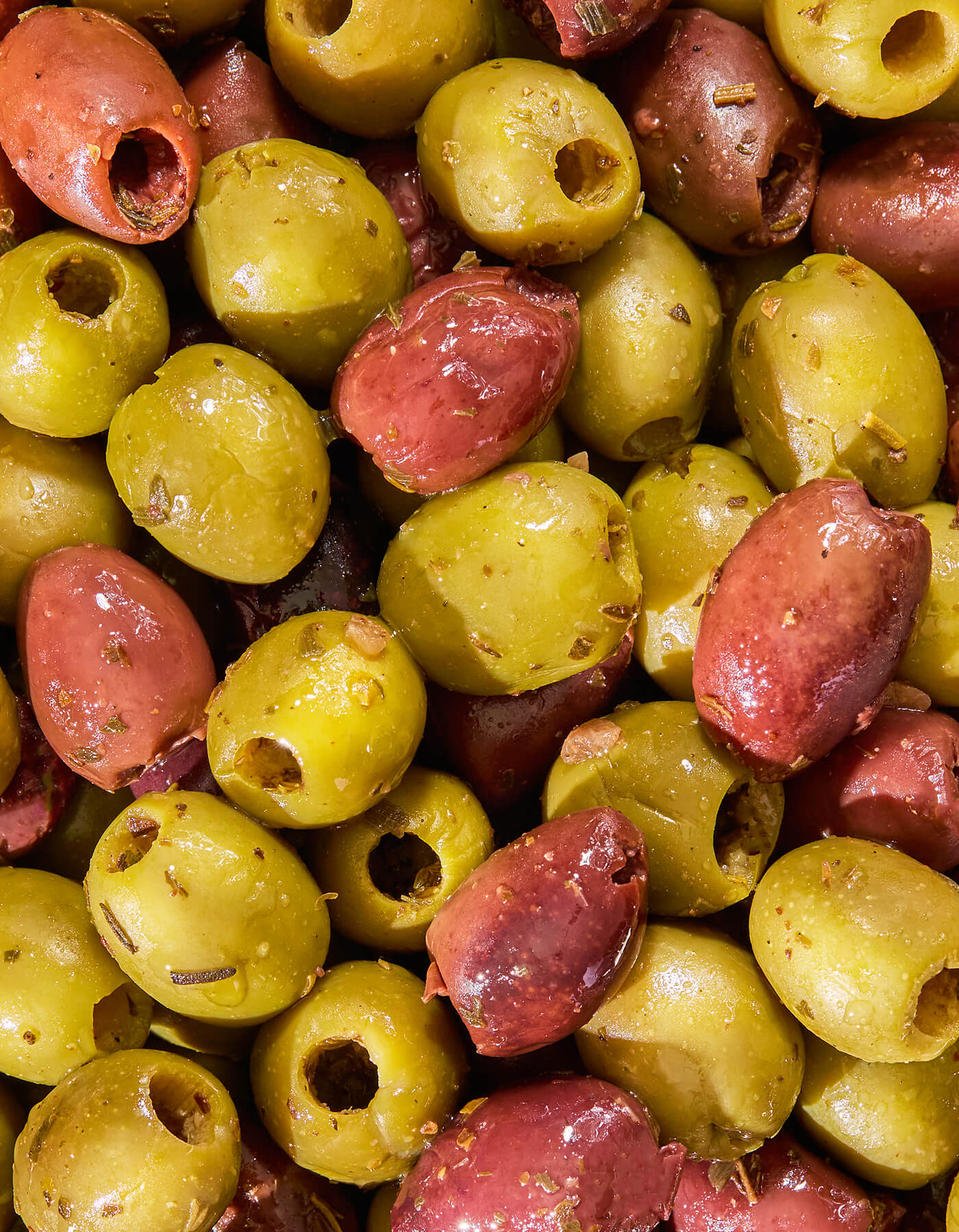 Close-up of a mix of green and red olives coated in herby goodness.