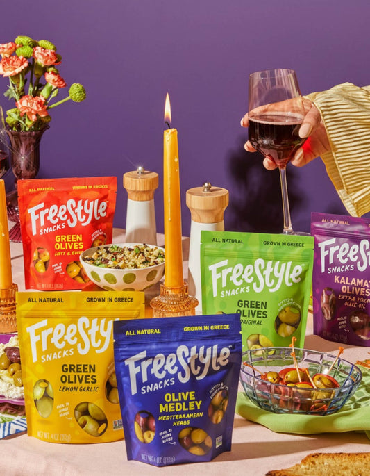 Freestyle Snacks packaging on a table with a person holding a glass of wine.