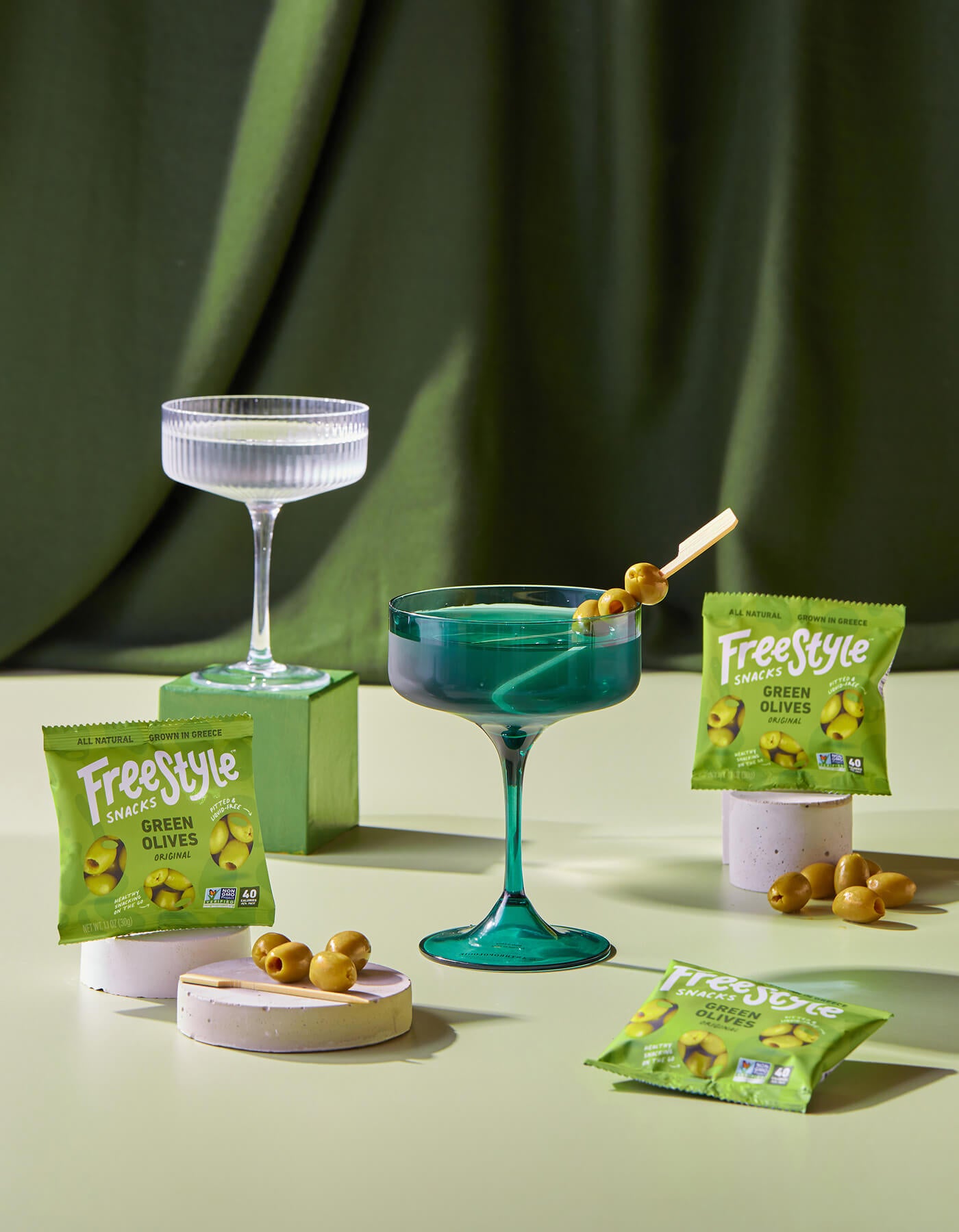 Green cocktail with olives and Freestyle branded packaging on a green background