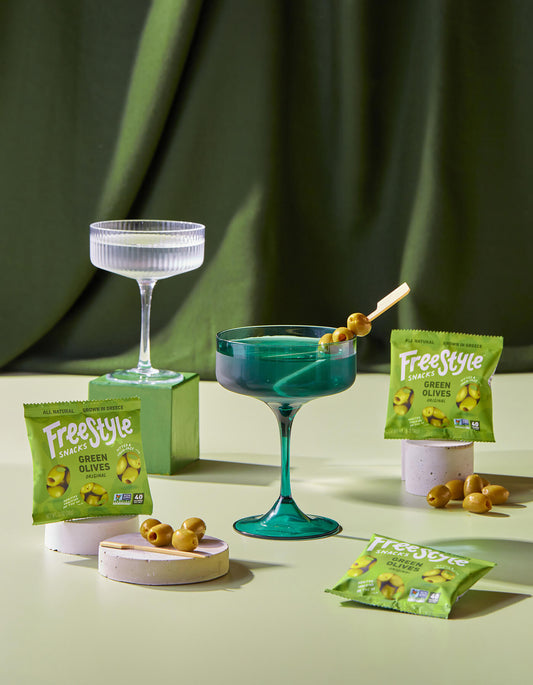 Green cocktail with olives and Freestyle branded packaging on a green background